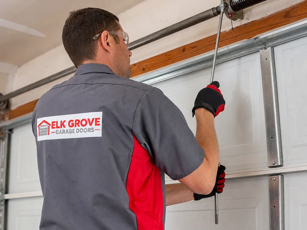 Contractor using winding bars to adjust torsion spring tension on a residential garage door torsion shaft